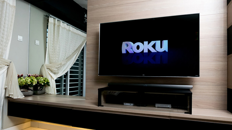 A TV against a wall and mirror shows the famous Roku logo against a black background.