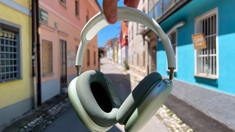 hand holding AirPods Max with narrow city street in the background