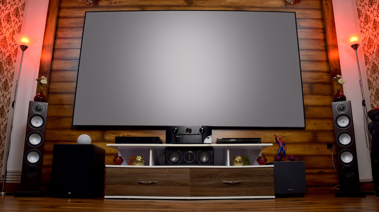 Room with wood paneling, featuring a large TV and an audio system with speakers and subwoofer.