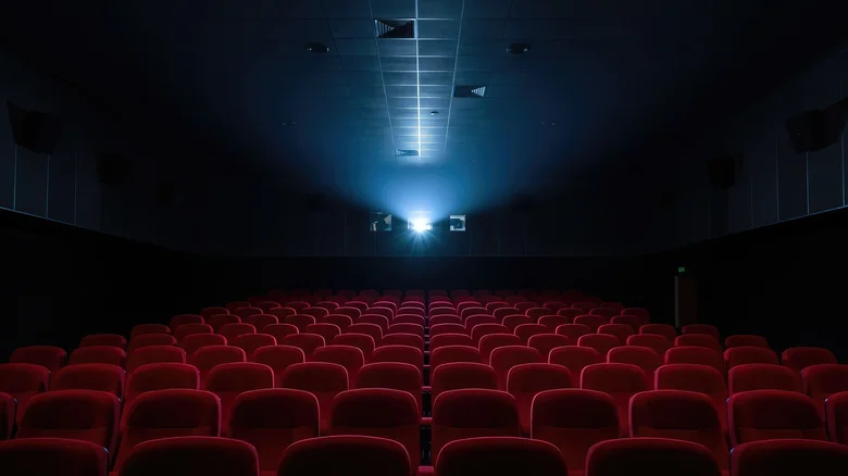 Empty cinema with row upon row of empty red seats, with the bright glare of the projector in the back.