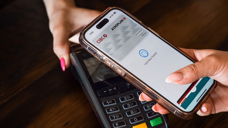 A person holding an iPhone using Apple Pay near a card reader.