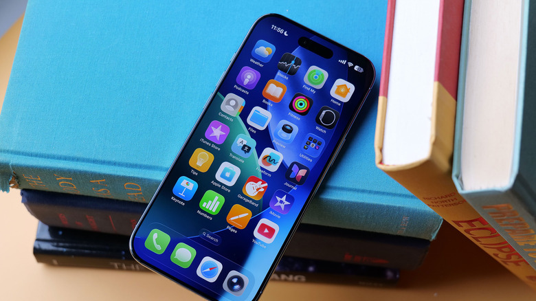 An iPhone leaning diagonally on a stack of books.