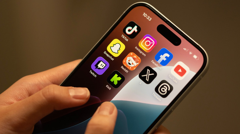 Close-up shot of person holding an iPhone displaying popular social media apps.