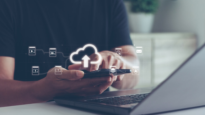 A person using a phone in front of a laptop with a glowing cloud icon overlaid.
