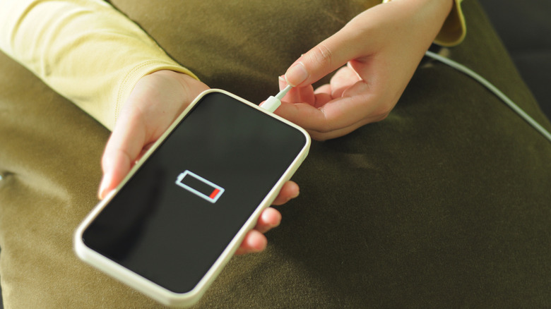 A hand holding a phone showing the a small red amount of battery on the screen, and plugging it in.