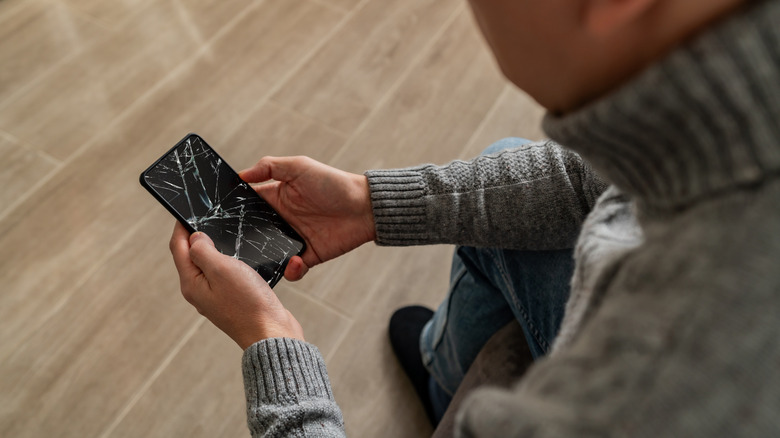 A person looks at a smartphone with a cracked display.