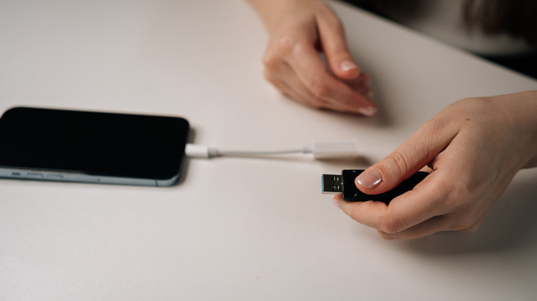 Person holding a USB flash drive, ready to connect it to an iPhone with a USB adapter