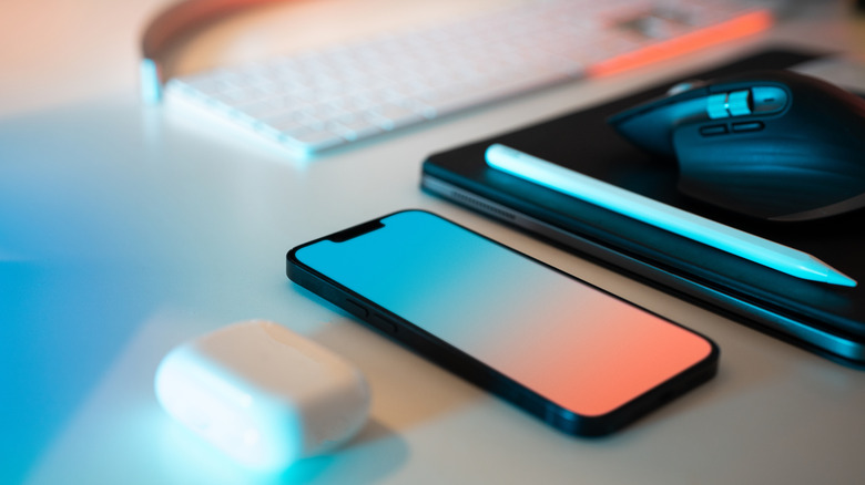 An iPhone next to an iPad with an Apple Pencil and mouse on top of it.