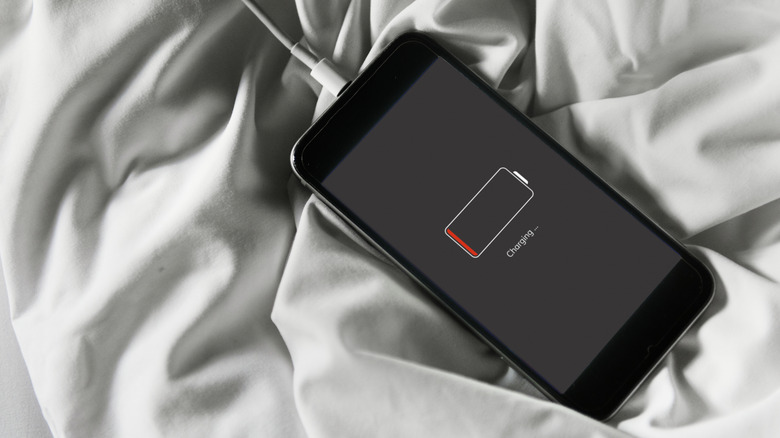 A phone on a crinkled blanket showing a dead battery and charging.