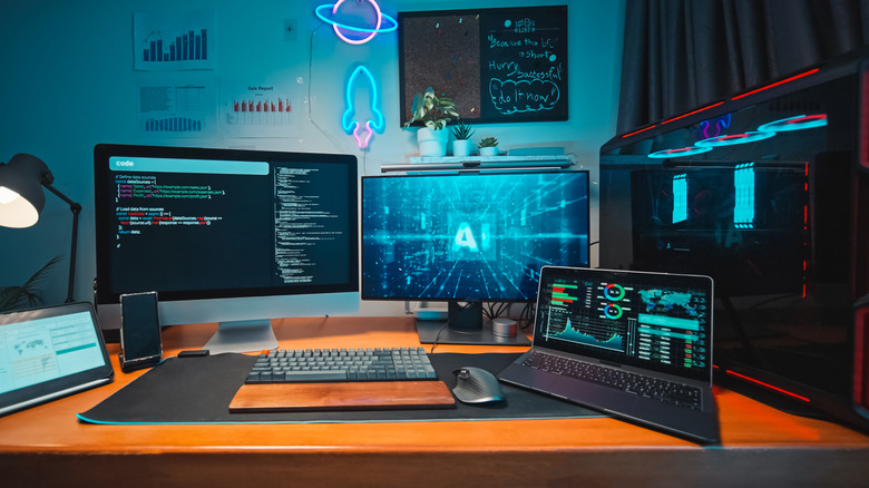 A multi-monitor desktop PC setup at a desk, with an additional laptop and smartphone stand.