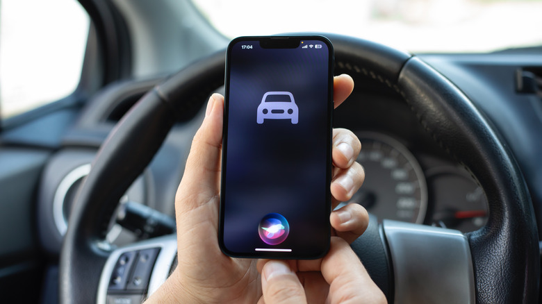 The Driving Focus icon on an iPhone with the Siri icon, in front of a car steering wheel.