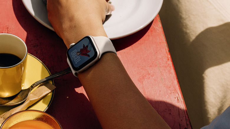 A wrist wearing the Apple Watch SE on a patio with coffee.