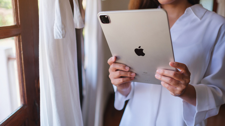 A woman holding an iPad in front of a window with white curtains.