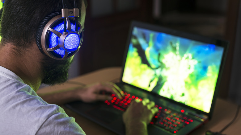 A man wearing headphones playing on a gaming laptop.