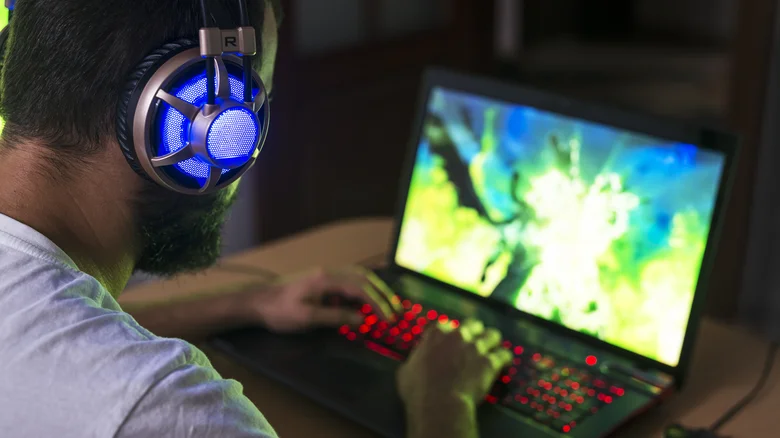 A man wearing headphones playing on a gaming laptop.