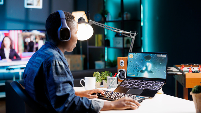 A woman playing a space sim on a gaming laptop.