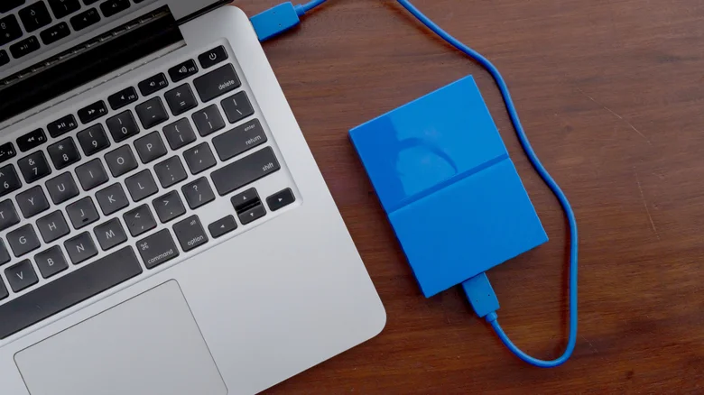 A bright blue external SSD plugged into a MacBook's USB port.