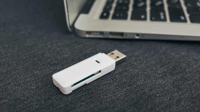 A white USB thumb drive next to a MacBook Air.
