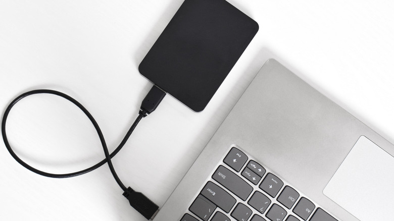A black external hard drive plugged into a silver laptop.