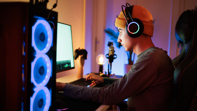 A guy wearing headphones while sitting at his desk playing on a PC.
