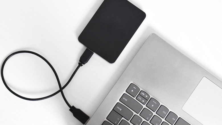 A black external hard drive plugged in to a silver laptop.