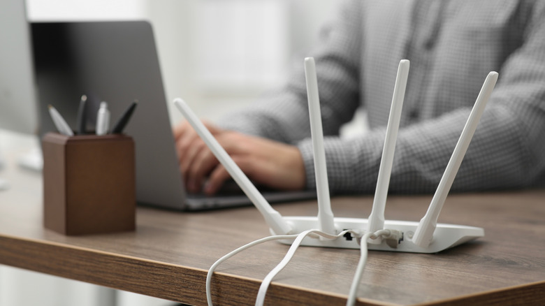 A man working on a laptop at a desk that also has a white router on it.