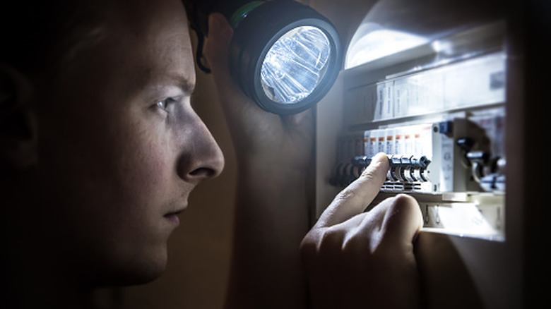 Man with flashlight checking out an electrical panel.