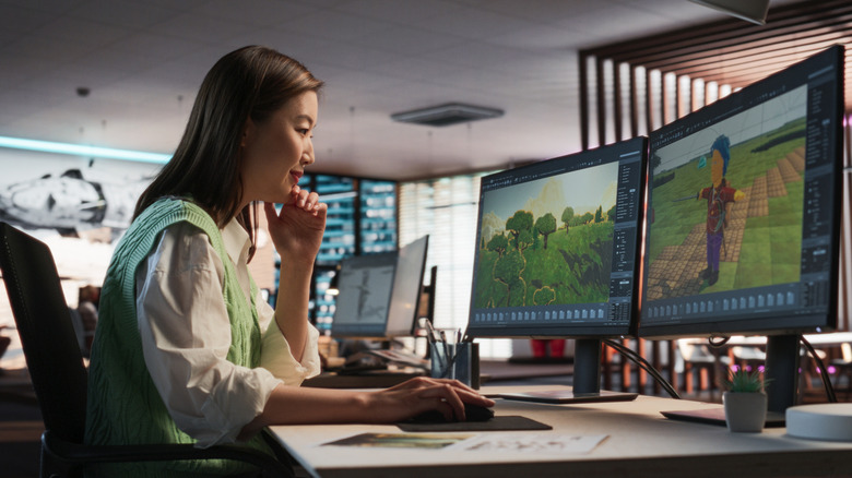 A woman editing character and world mdoels for a game on dual monitors