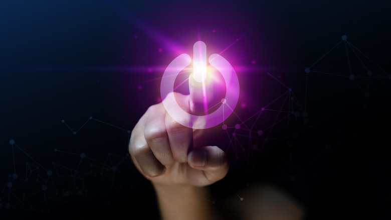 A hand pressing a large, illuminated, purple power button on an otherwise blank surface.