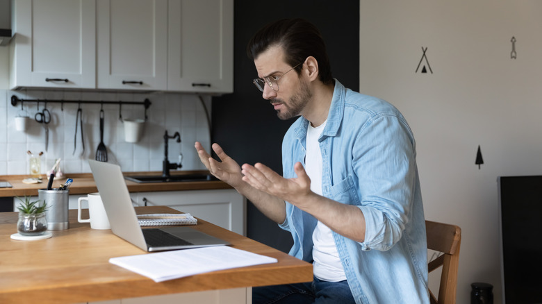 A man holding up his hands in frustration to his laptop.