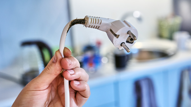 A hand holding up the cord and plug of a white extension cord that has shorted.