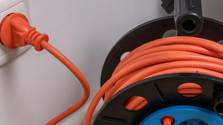 An orange extension cord wrapped around a cable reel and plugged into a wall outlet.