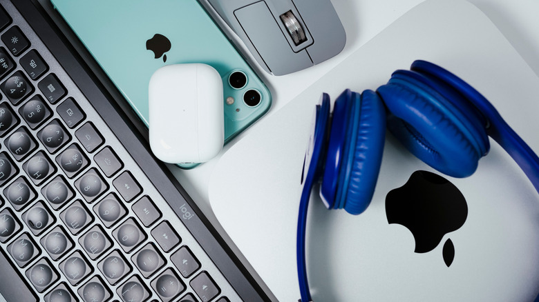 AirPods sitting on top of an iPhone next to a Mac mini, AirPods Max and a keyboard/mouse.