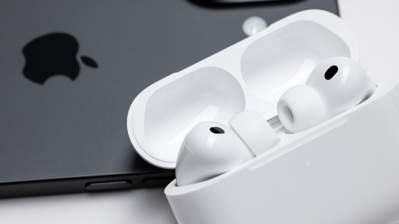 An iPhone next to AirPods with the charging case lid open.
