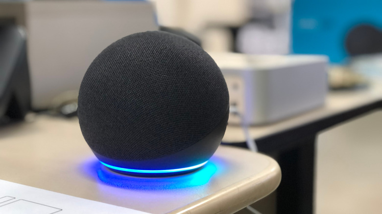 An Amazon Echo Dot speaker placed on a table, with its blue light glowing.