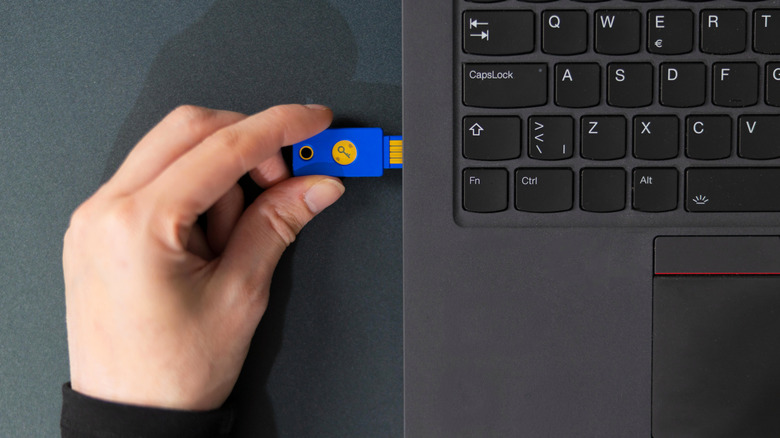 Hand plugging a blue security key into a USB port on the side of a laptop.