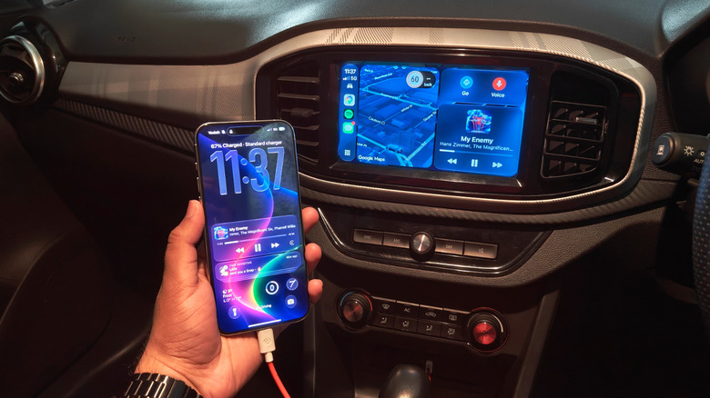 A hand holding a phone using CarPlay with a wired connection.