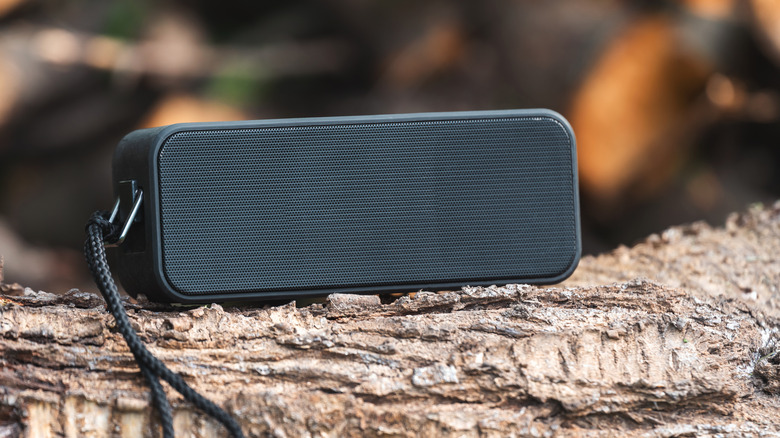 A portable black Bluetooth speaker resting on a tree trunk outdoors.