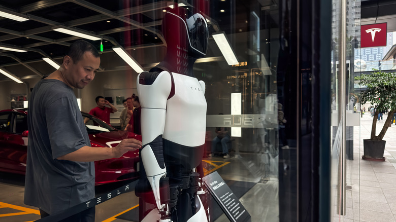 Tesla's Optimus humanoid robot is displayed inside a Tesla store as a visitor stands nearby.