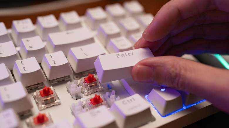 Hand inserting keycap into keyboard.