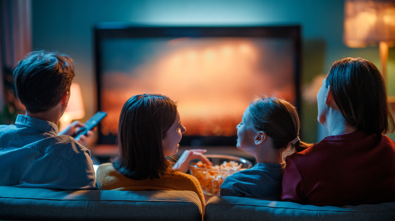 A family eats popcorn and flips through the channels of their large television.