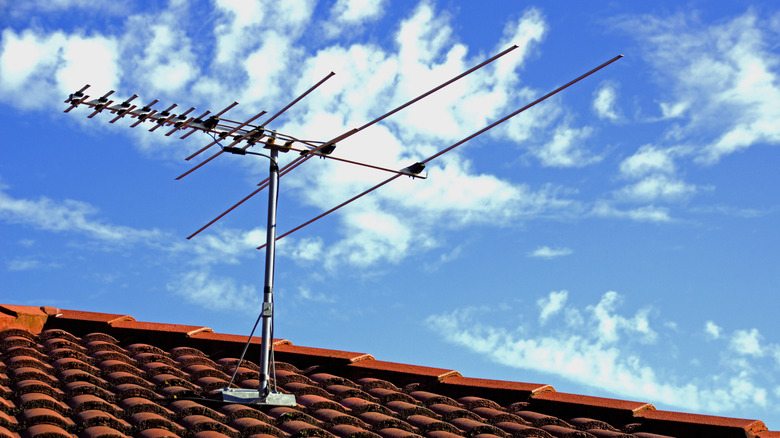 An outdoor TV antenna sits atop of a shingled roof on a sunny day.