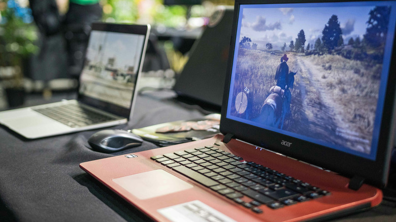 An old Acer laptop running Red Dead Redemption. Another laptop (blurred) is visible behind.