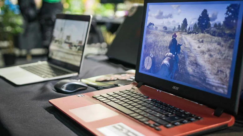 An old Acer laptop running Red Dead Redemption. Another laptop (blurred) is visible behind.