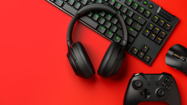 Black headphones, gaming controller and keyboard on red background