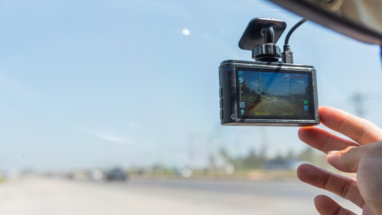 A person touching a button on a dash cam mounted on the windshield of a car.