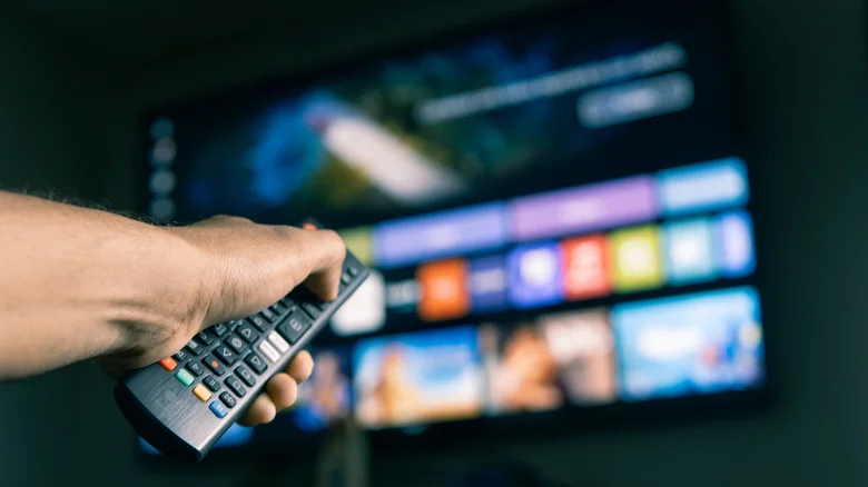 A hand holding a remote control pointed at a television.