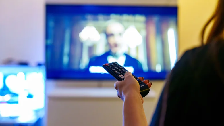 A hand holding a Samsung remote to control a smart TV.