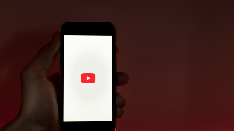 A YouTube logo on a smartphone with a human hand.