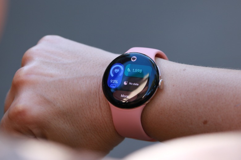 The peach Pixel Watch 5 held up on a person's wrist showing the daily activity progress dashboard.